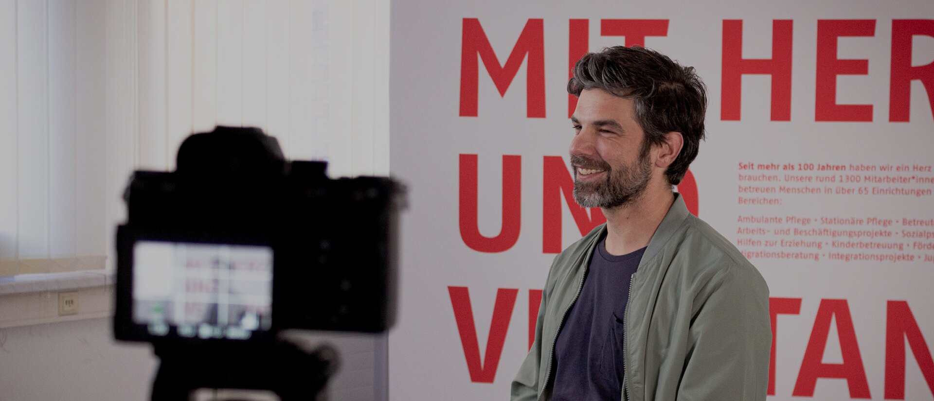 Das Foto zeigt einen Mann mittleren Alters, der vor einer Kamera sitzt